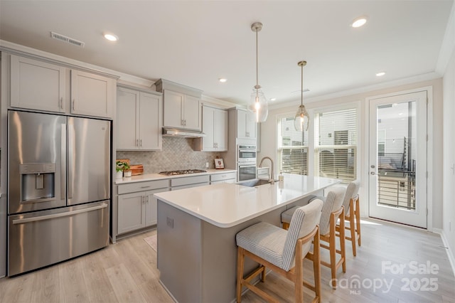 kitchen featuring pendant lighting, gray cabinets, a breakfast bar, appliances with stainless steel finishes, and a kitchen island with sink