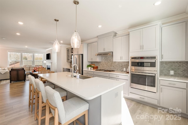 kitchen featuring a breakfast bar area, appliances with stainless steel finishes, hanging light fixtures, ornamental molding, and a center island with sink