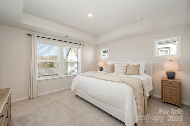 bedroom with multiple windows, a raised ceiling, and light carpet