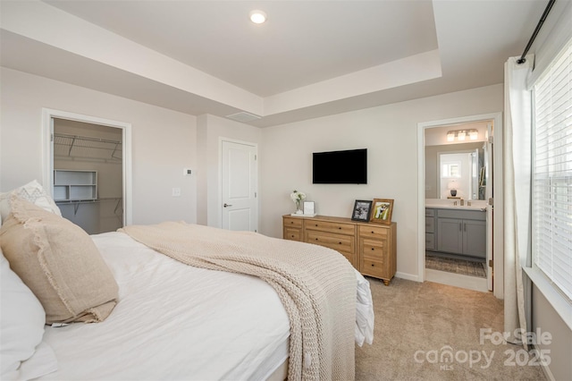 bedroom with sink, ensuite bath, a tray ceiling, light carpet, and a walk in closet