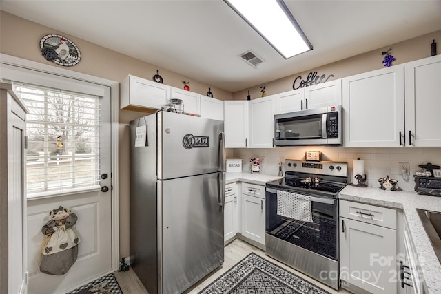 kitchen featuring decorative backsplash, light stone counters, white cabinetry, and appliances with stainless steel finishes