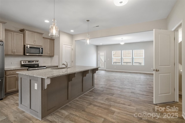 kitchen featuring pendant lighting, appliances with stainless steel finishes, a kitchen bar, an island with sink, and sink