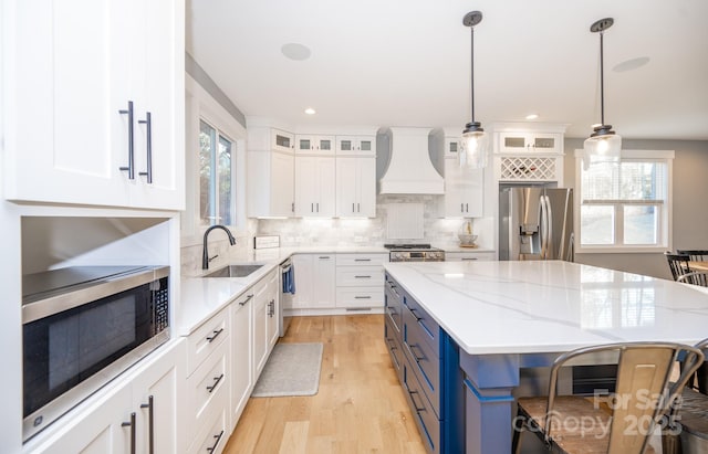 kitchen featuring decorative light fixtures, custom exhaust hood, sink, stainless steel appliances, and white cabinets