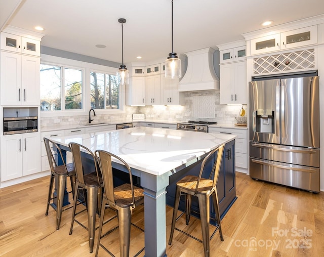 kitchen with light hardwood / wood-style floors, custom exhaust hood, a center island, hanging light fixtures, and appliances with stainless steel finishes