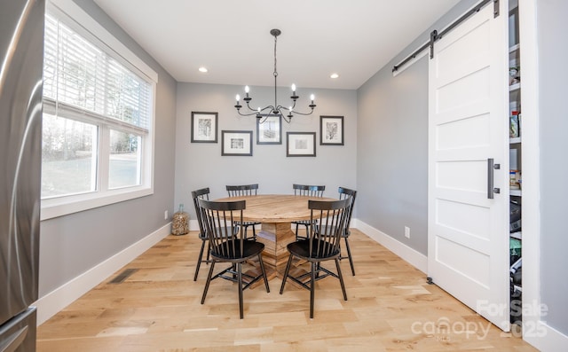 dining space featuring a notable chandelier, a barn door, and light hardwood / wood-style flooring