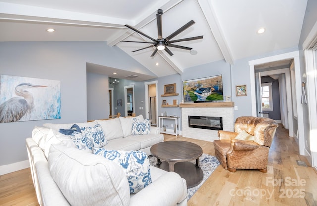 living room featuring light hardwood / wood-style floors, ceiling fan, a stone fireplace, and vaulted ceiling with beams