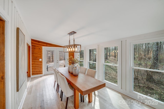 dining space featuring vaulted ceiling, wood walls, light hardwood / wood-style floors, an inviting chandelier, and french doors