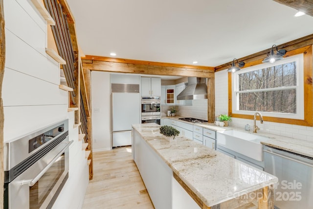 kitchen with a kitchen island, white cabinetry, light stone counters, stainless steel appliances, and wall chimney range hood