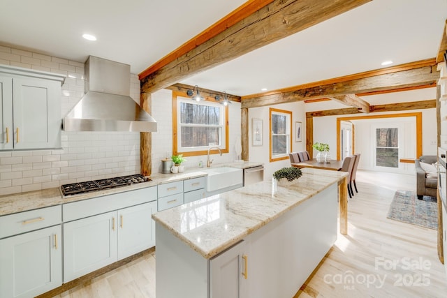 kitchen featuring wall chimney exhaust hood, sink, light stone counters, a center island, and stainless steel appliances