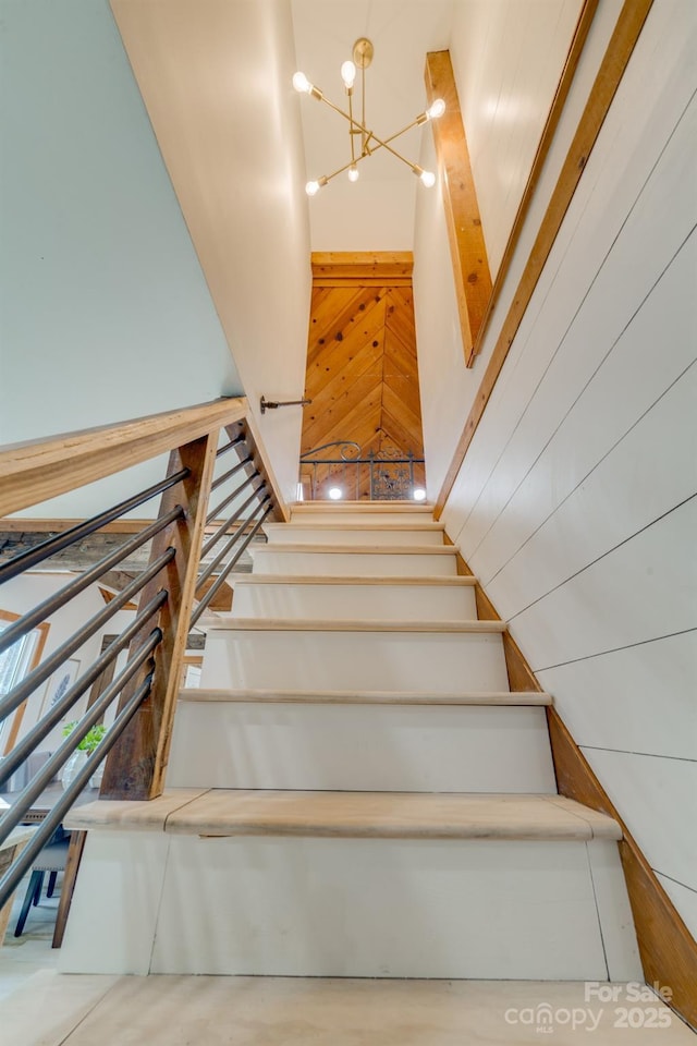 staircase with a notable chandelier, a towering ceiling, and wood walls