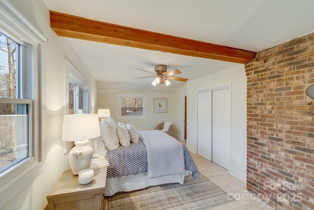 bedroom with light hardwood / wood-style floors, brick wall, beam ceiling, and a closet