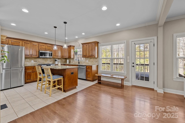 kitchen with appliances with stainless steel finishes, light stone counters, ornamental molding, a kitchen island, and decorative light fixtures