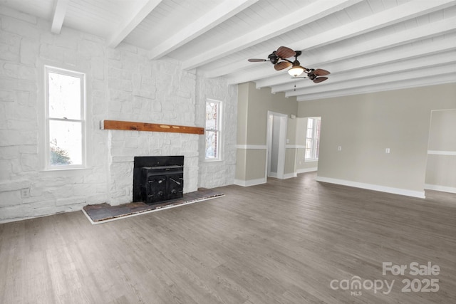 unfurnished living room featuring hardwood / wood-style flooring, ceiling fan, a stone fireplace, and beamed ceiling