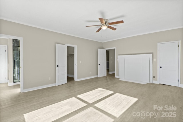 unfurnished bedroom featuring ceiling fan, a spacious closet, ornamental molding, and light hardwood / wood-style flooring