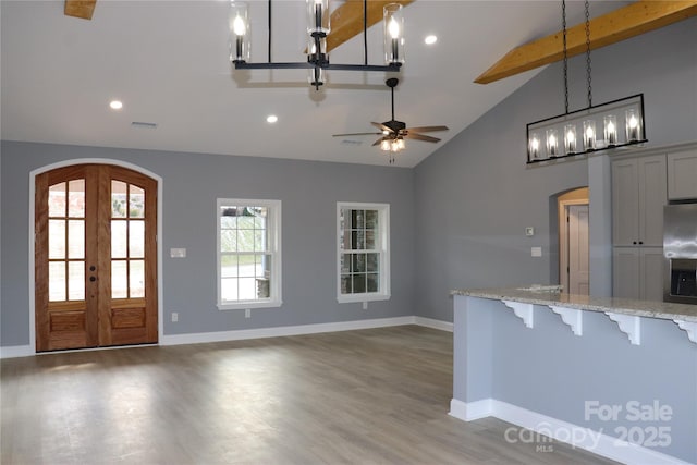 kitchen featuring french doors, a breakfast bar area, light stone counters, hanging light fixtures, and beamed ceiling