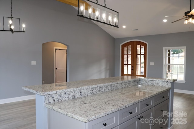 kitchen featuring hanging light fixtures, a kitchen island, light stone counters, and french doors