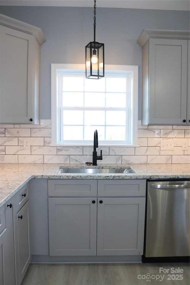 kitchen featuring pendant lighting, sink, dishwasher, light stone counters, and decorative backsplash