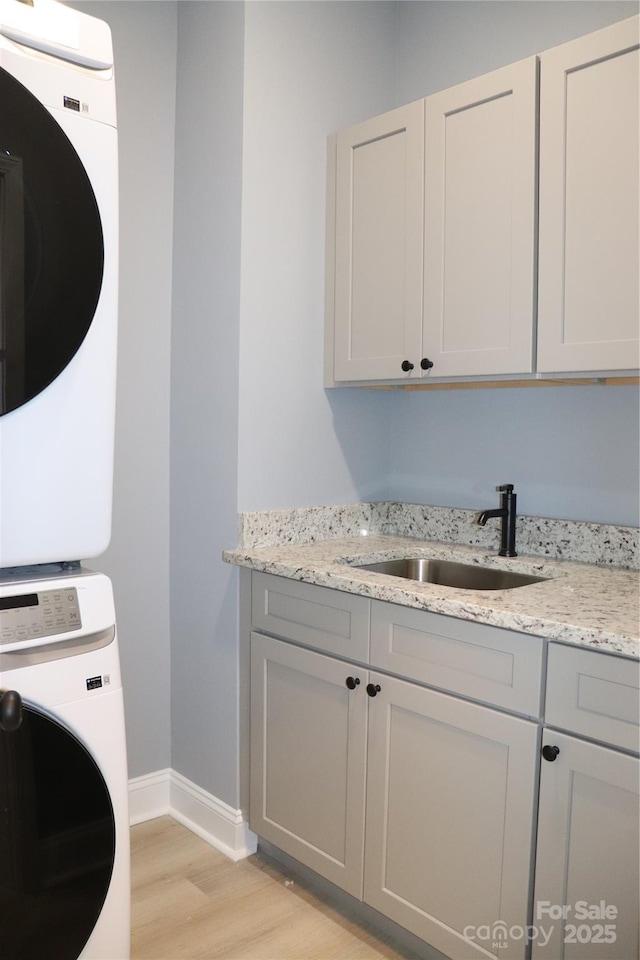 washroom with cabinets, stacked washer / drying machine, sink, and light wood-type flooring