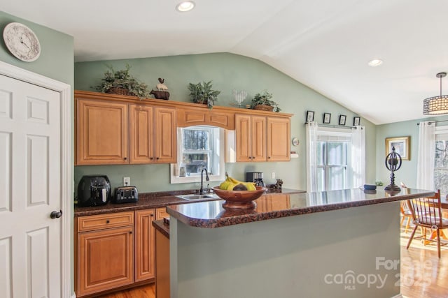 kitchen with vaulted ceiling, a kitchen island, pendant lighting, sink, and light wood-type flooring