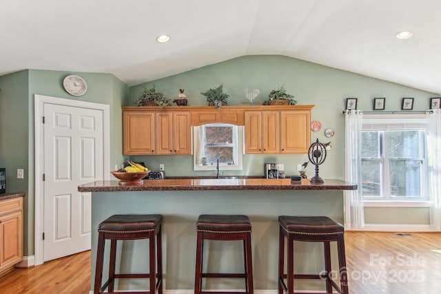 kitchen featuring light hardwood / wood-style floors, a kitchen bar, lofted ceiling, a kitchen island, and sink