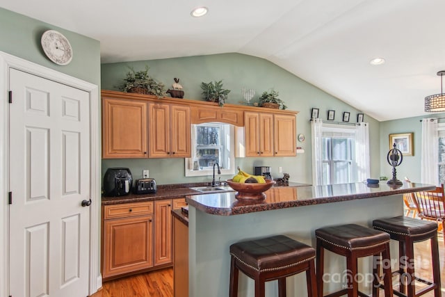 kitchen with light hardwood / wood-style floors, vaulted ceiling, a kitchen island, pendant lighting, and sink