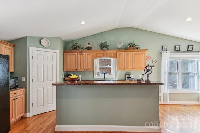 kitchen with light wood-type flooring, a kitchen island, vaulted ceiling, and black appliances