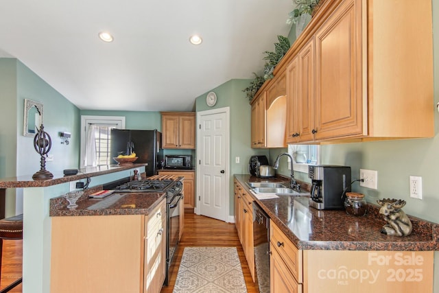 kitchen with black appliances, a kitchen bar, light brown cabinets, sink, and light wood-type flooring