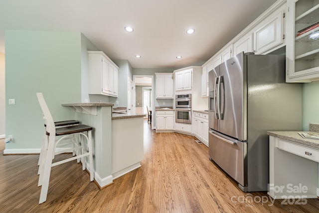 kitchen with light hardwood / wood-style flooring, appliances with stainless steel finishes, a kitchen breakfast bar, light stone countertops, and white cabinets