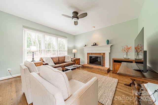 living room with ceiling fan, a brick fireplace, and light wood-type flooring