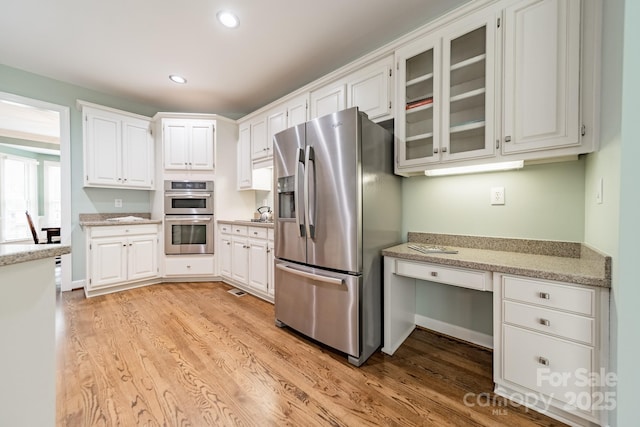 kitchen featuring white cabinetry, stainless steel appliances, built in desk, and light wood-type flooring