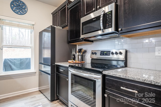 kitchen featuring appliances with stainless steel finishes, decorative backsplash, light stone counters, and light hardwood / wood-style flooring