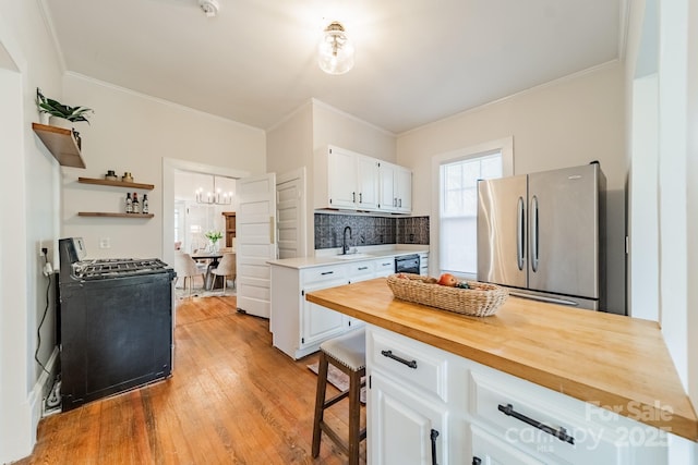 kitchen with white cabinets, range with gas stovetop, decorative backsplash, stainless steel fridge, and butcher block countertops