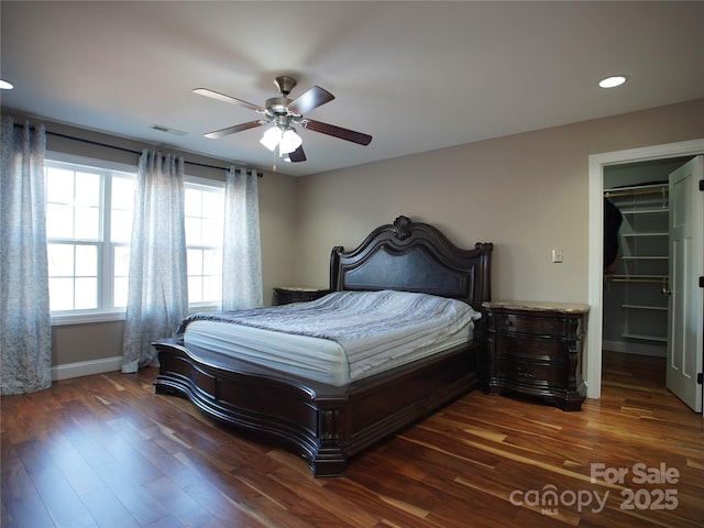 bedroom with a closet, ceiling fan, a spacious closet, and dark wood-type flooring