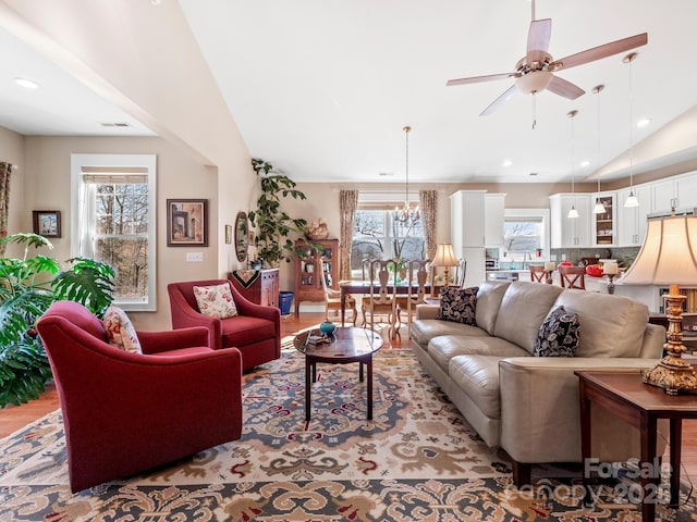 living room featuring light wood-type flooring, ceiling fan with notable chandelier, and lofted ceiling