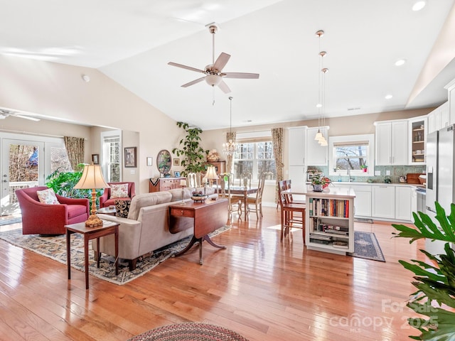 living room with ceiling fan, light hardwood / wood-style flooring, and vaulted ceiling