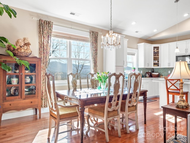 dining area with an inviting chandelier, lofted ceiling, and light wood-type flooring