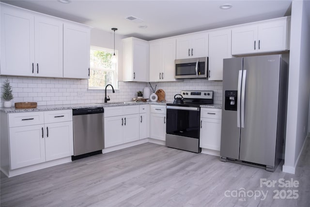 kitchen with white cabinets, stainless steel appliances, light hardwood / wood-style floors, sink, and hanging light fixtures