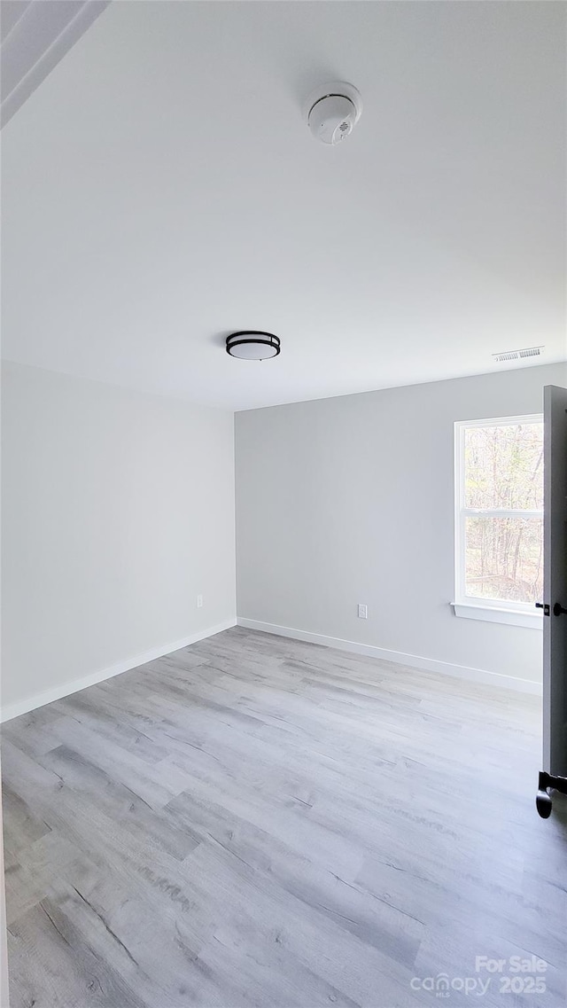 empty room featuring wood finished floors, visible vents, and baseboards