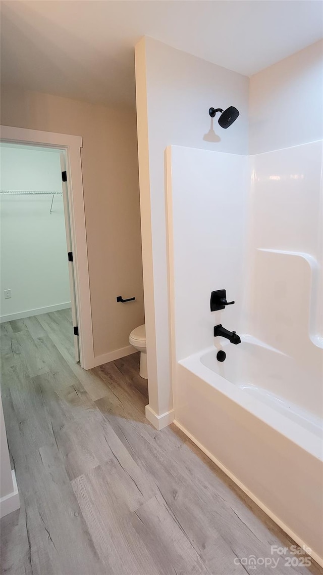 bathroom featuring baseboards, toilet, shower / tub combination, wood finished floors, and a spacious closet