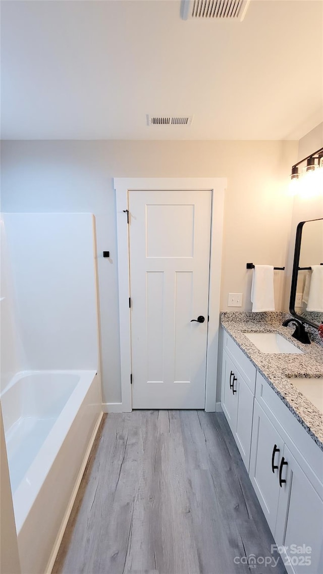 bathroom with visible vents, vanity, a bath, and wood finished floors