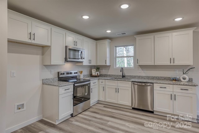 kitchen featuring stainless steel appliances, a sink, visible vents, white cabinets, and light wood-type flooring