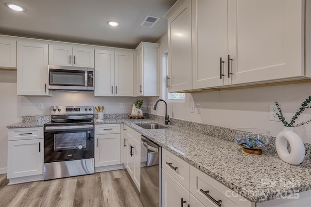 kitchen featuring visible vents, appliances with stainless steel finishes, light wood-style floors, white cabinetry, and a sink