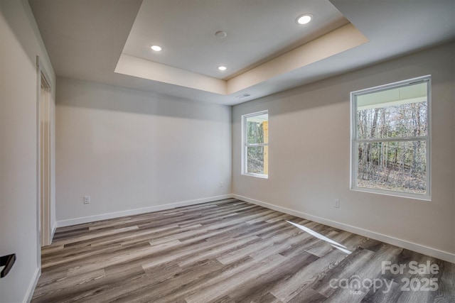 spare room with a tray ceiling, recessed lighting, baseboards, and wood finished floors