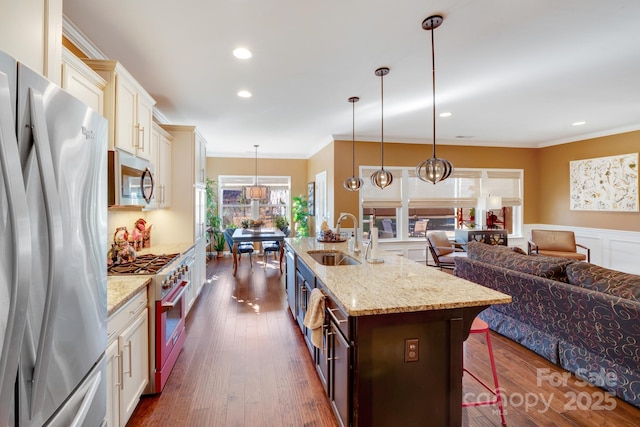 kitchen with sink, appliances with stainless steel finishes, hanging light fixtures, light stone countertops, and an island with sink