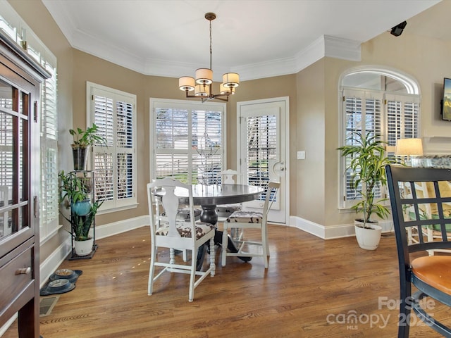 dining area with a notable chandelier, ornamental molding, and dark hardwood / wood-style floors