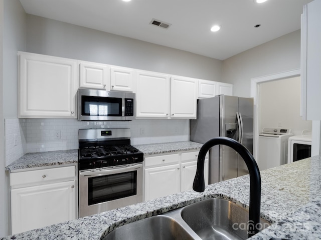 kitchen with sink, washer and clothes dryer, appliances with stainless steel finishes, light stone countertops, and white cabinets