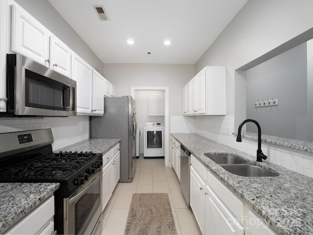 kitchen with washer / dryer, sink, light stone counters, stainless steel appliances, and white cabinets