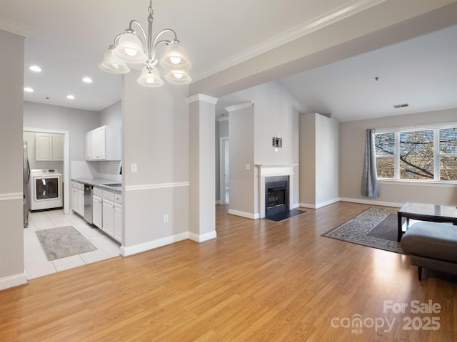 unfurnished living room featuring an inviting chandelier, washer / clothes dryer, ornamental molding, and light wood-type flooring