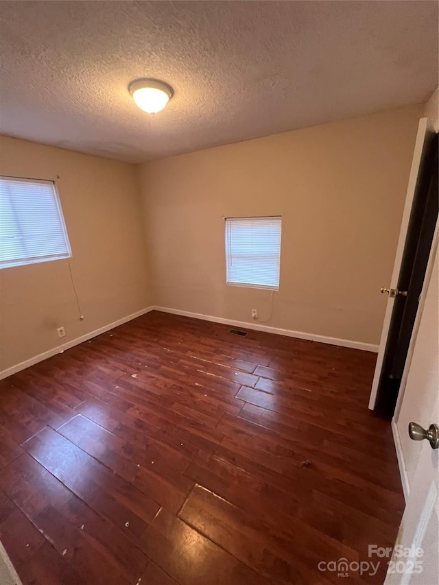 empty room with dark hardwood / wood-style flooring and a textured ceiling