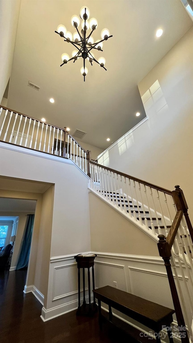 stairway with wood-type flooring, a towering ceiling, and a notable chandelier